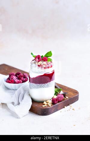 Marmellata di lamponi, budino di chia e yogurt. Condito con granola per fare un parfait in un vaso di vetro. Foto Stock