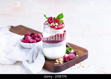 Marmellata di lamponi, budino di chia e yogurt. Condito con granola per fare un parfait in un vaso di vetro. Foto Stock