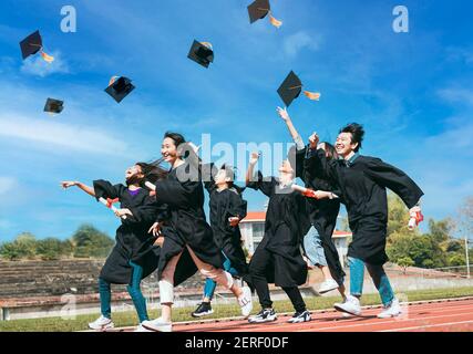 Felici gli studenti con le congratulazioni che gettano i cappelli di laurea in aria per festeggiare Foto Stock