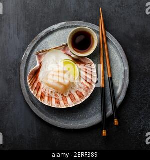 Sashimi vivi al capesante su conchiglia con salsa di daikon, lime e soia su fondo scuro Foto Stock