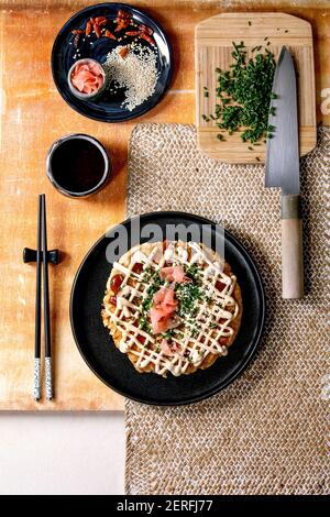 Frittella di cavolo okonomiyaki giapponese fatta in casa decorata con cipollina, zenzero sottaceto, salsa mayo su piastra di ceramica nera con chopsticks A. Foto Stock