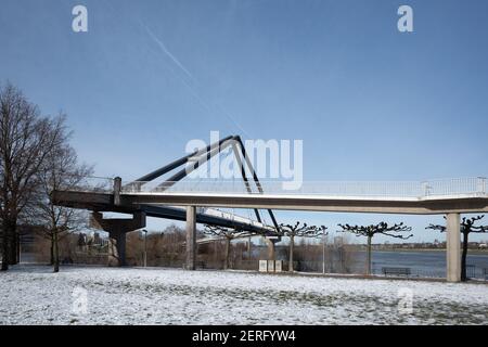 Vista soleggiata all'aperto di Fussgängerbrücke, ponte pedonale, a Rheinpark Bilk e campo coperto di neve sulla passeggiata del fiume Reno nella stagione invernale. Foto Stock