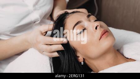 primo piano della foto di una sessione di massaggio alla testa eseguita a. il centro termale ad una donna di brunette che si trova con chiuso occhi Foto Stock