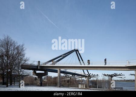 Vista soleggiata all'aperto di Fussgängerbrücke, ponte pedonale, a Rheinpark Bilk e campo coperto di neve sulla passeggiata del fiume Reno nella stagione invernale. Foto Stock