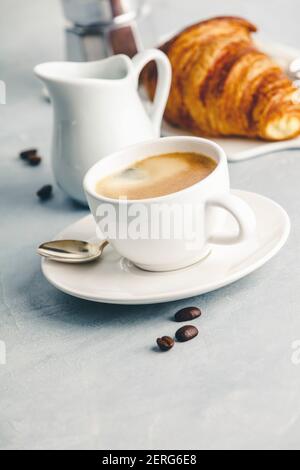 Composizione del caffè sul cemento bianco sullo sfondo. Caffè espresso in tazza bianca con latte, marmellate e croissant. Concetto di colazione Foto Stock