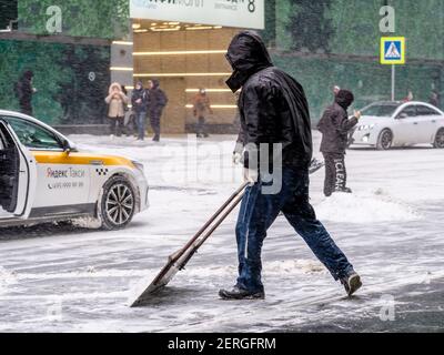 Mosca. Russia. 12 febbraio 2021. Un addetto alla pubblica utilità rimuove la neve con uno scraper su una strada cittadina durante una nevicata in una giornata invernale. labo fisico duro Foto Stock