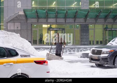 Mosca. Russia. 12 febbraio 2021. Un addetto alla pubblica utilità rimuove la neve con uno scraper su una strada cittadina durante una nevicata in una giornata invernale. labo fisico duro Foto Stock