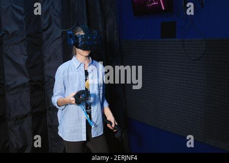 Ragazza teenager che usa il visore per la realtà virtuale nella stanza buia del club di gioco vr. Concetto di simulazione virtuale, gioco, internet delle cose. Foto Stock