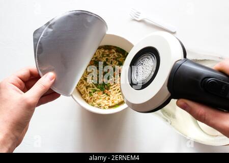uomo versando acqua bollente su tagliatelle istantanee Foto Stock