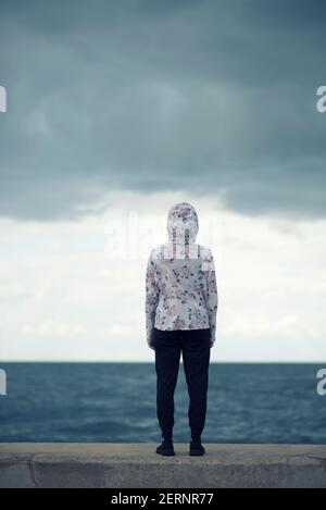 Vista posteriore della donna che indossa una felpa con cappuccio floreale in piedi sul spiaggia Foto Stock