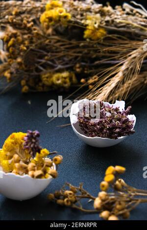 Fai da te di Pasqua. Fai da te. Decorazioni pasquali alla moda. Uova biologiche cracked con erba secca e fiori secchi su piatto. Piuma d'uccello. Spazio di copia. Biglietto d'auguri. Sfondo scuro. Foto Stock