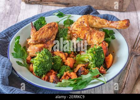 pasto di pollo con patate e verdure servite su un piatto su tavolo rustico Foto Stock