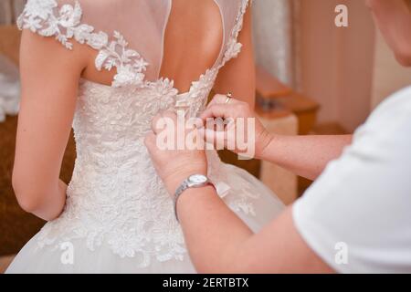 La madre della sposa aiuta la sposa a vestirsi. Foto Stock