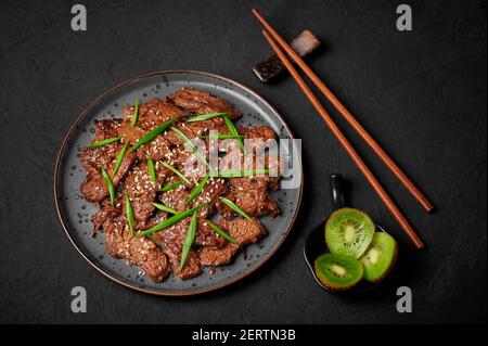 Borgogi di manzo su piastra nera su piano tavolo di ardesia scuro. Piatto di carne della cucina coreana con salsa e kiwi. Cucina asiatica tradizionale Foto Stock