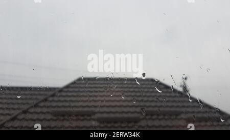 Il finestrino in caso di pioggia si abbassa. Gocce d'acqua sul vetro. Tetto sullo sfondo Foto Stock
