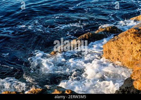 Onde che si infrangono sulle rocce sulla spiaggia al mattino. Alba sul mare ondulato con rocce Foto Stock