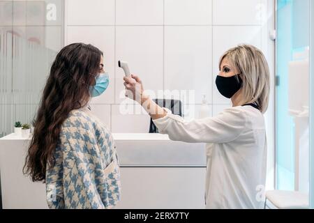 Foto di scorta di un assistente di clinica odontoiatrica che usa un termometro per controllare la temperatura corporea per verificare la presenza di sintomi di virus. Foto Stock