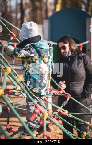 POZNAN, POLONIA - 21 feb 2021: Donna con occhiali da sole in piedi da un ragazzo su una griglia di corda attrezzatura per salire in un parco giochi nel Solacki Park. Relat Foto Stock