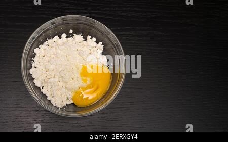 Formaggio di cottage granuloso, uovo in un recipiente di vetro su un tavolo nero primo piano con spazio copia, vista dall'alto Foto Stock