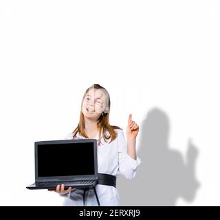 Una bionda contenta tiene un computer portatile e punta il dito verso l'alto in uno spazio vuoto dove il testo o la pubblicità potrebbe essere. Idea su un bianco Foto Stock