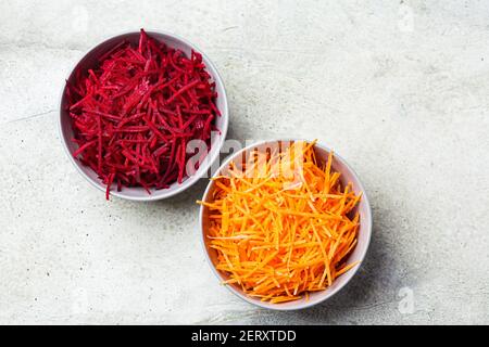 Barbabietole e carote tritate in ciotole grigie. Ingredienti per una cucina sana. Foto Stock