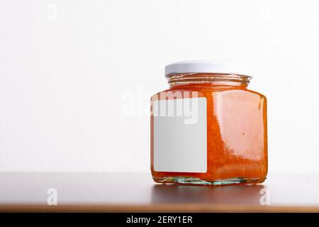 Succosa marmellata di carote fatte in casa in vaso di vetro su uno sfondo di tavolo, modello di serie mock-up modificabile pronto per il tuo design, percorso di selezione etichetta incluso. Foto Stock
