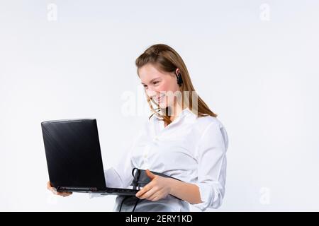 Giovane donna di affari sorride felicemente e comunica attraverso la comunicazione video mentre tiene un laptop in mano. Sfondo bianco. Foto Stock