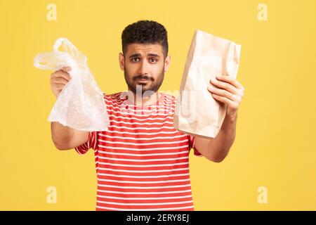 Uomo serio bearded in t-shirt a righe che tiene fuori le mani con carta e sacchetto di poly, dandogli la possibilità di fare la scelta giusta e salvare il pianeta. studi interni Foto Stock