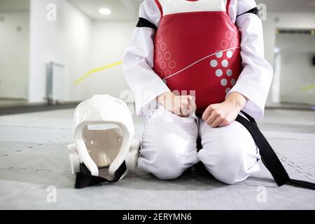 Artista marziale in abbigliamento protettivo seduto e tenendo un casco, cintura nera, uniforme bianca, taekwondo Foto Stock