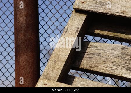 Closeup vecchio pallet di legno vicino ad una recinzione di rete arrugginita Foto Stock