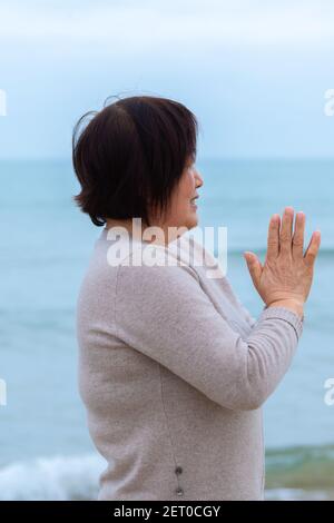 Donna matura che pratica la meditazione vicino al mare Foto Stock