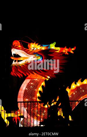 Il Festival cinese delle Lanterne. Una lanterna cinese del drago è in piedi dietro la recinzione, e una silhouette di una donna con un carrello del bambino. Foto Stock
