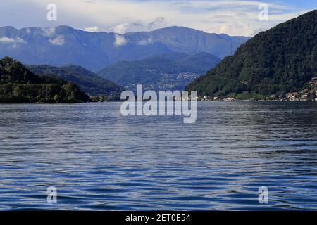 Panorama del Lago di Lugano con montagne, alberi, città e nuvole Foto Stock