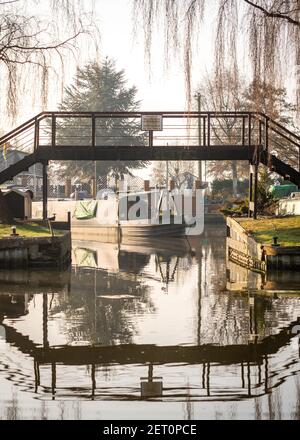 Rustico vecchio canale stretta casa barca ormeggiata in molo con passerella sopra il fiume che si riflette in calma acqua ancora a. marina per lavori di restauro Foto Stock