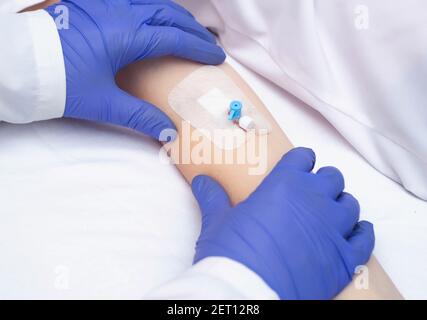 Un medico in guanti medici tiene la mano del paziente con un catetere endovenoso. Concetto di malattie del sangue umano, leucemia, biochimica Foto Stock