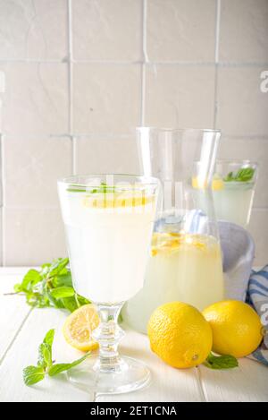 Bevanda ghiacciata fatta in casa con limonata, cocktail liquore al limoncello decorato con menta e limoni su sfondo bianco della cucina in legno Foto Stock