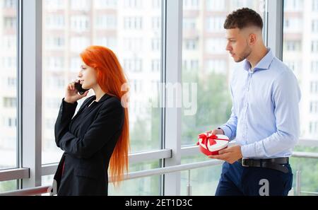 Uomo d'affari sorpresa e dare scatola regalo rossa per uomo d'affari in ufficio per compleanno. Foto Stock