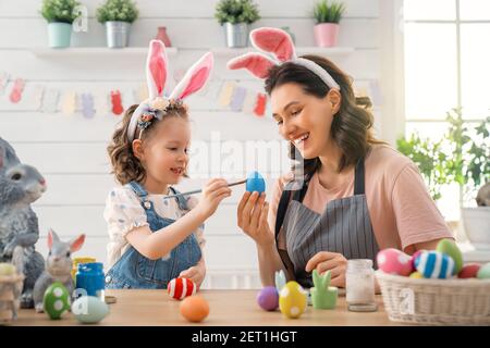 Madre e figlia dipingere le uova. La famiglia felice la preparazione per la Pasqua. Grazioso fanciullo ragazza indossando orecchie di coniglietto. Foto Stock