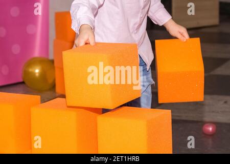 grandi blocchi arancioni di paralon nel centro per bambini, il bambino costruisce un muro a base di morbidi cubi. Foto Stock