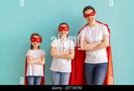 Madre e i suoi figli giocano insieme. Ragazze e mamma in costumi Superhero divertendosi e sorridendo. Vacanza in famiglia e insieme. Foto Stock