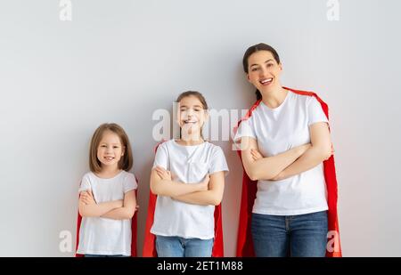 Madre e i suoi figli giocano insieme. Ragazze e mamma in costumi Superhero divertendosi e sorridendo. Vacanza in famiglia e insieme. Foto Stock