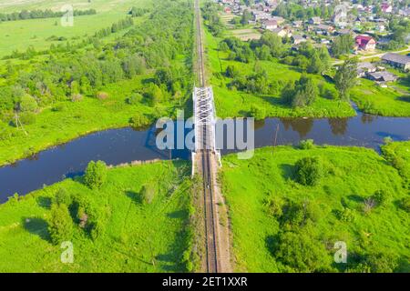 Ponte ferroviario tra prati verdi su un piccolo fiume in campagna, vista aerea Foto Stock