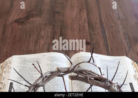 apri bibbia su tavola di legno scuro fondo centrale con parziale corona di spine che si stende sulla bibbia Foto Stock