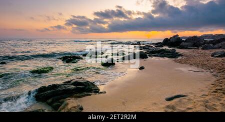 paesaggio marino all'alba. rocce sulla spiaggia sabbiosa. nuvole sul cielo. concetto di vacanza estiva Foto Stock