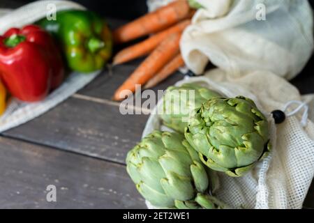 Vista closeup di carciofi freschi e verdure biologiche in sacchetti eco-riutilizzabili shopping su sfondo di legno.plastica libera, zero rifiuti concetto, sostenere Foto Stock