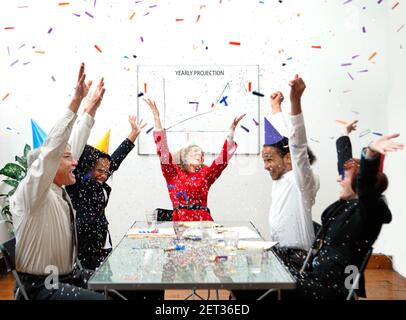 Gli uomini d'affari estatici celebrano un'eccellente proiezione annuale con cappelli e confetti da festa. Concetto di business umoristico. Foto Stock