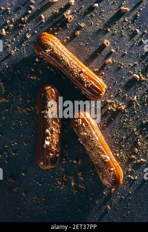 Tre eclair su un bancone disordinato scuro. Dolce torta francese. Disposizione piatta, vista dall'alto. Foto Stock