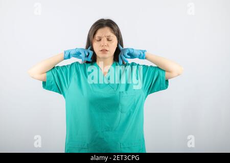 Giovane donna dottore in uniforme verde che copre le orecchie con indice dita Foto Stock