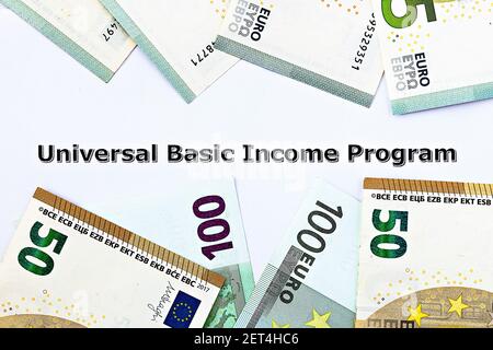 Foto in primo piano sul tema reddito base universale. Le parole programma di base universale del reddito sulla carta, circondato da banconote in euro Foto Stock