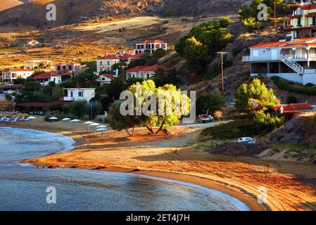 Piccola baia con spiaggia di sabbia, barche, case vacanze e alberi all'alba. Nella parte occidentale dell'isola di Lignos, Agios Ioannis, Grecia. Foto Stock